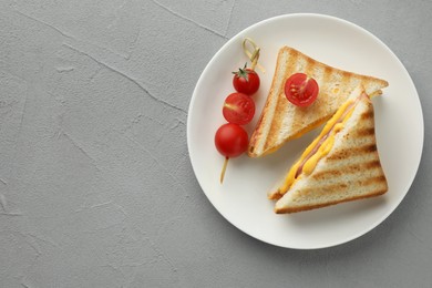 Tasty sandwiches with ham, melted cheese and tomatoes on grey textured table, top view. Space for text