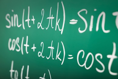 Many different math formulas written on green chalkboard, closeup
