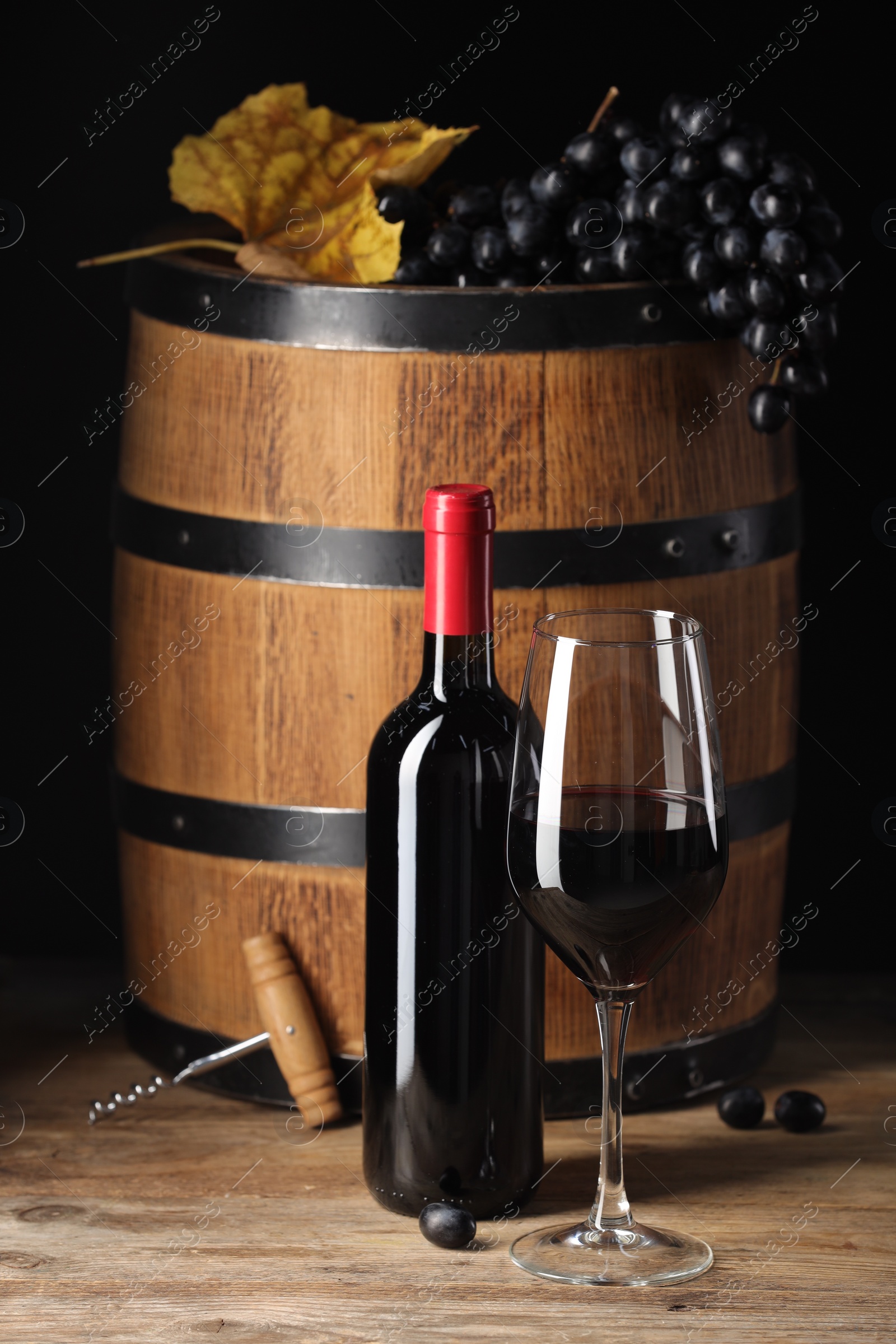 Photo of Delicious wine, wooden barrel and ripe grapes on table against black background