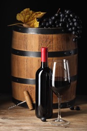 Delicious wine, wooden barrel and ripe grapes on table against black background