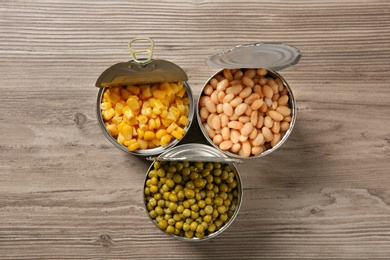 Photo of Open tin cans with different vegetables on wooden table, flat lay