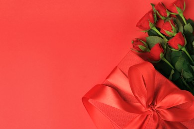 Photo of Beautiful gift box with bow and roses on red background, flat lay. Space for text