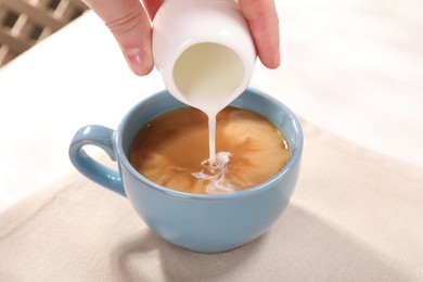 Woman pouring milk into cup with aromatic coffee at white table, closeup