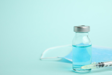 Photo of Vial, syringe and surgical mask on turquoise background, space for text. Vaccination and immunization