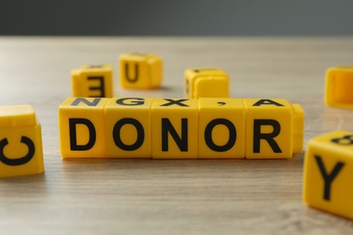 Word Donor made of yellow cubes on wooden table, closeup