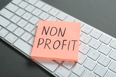 Photo of Paper note with phrase Non Profit and keyboard on grey background, closeup