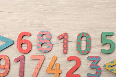 Colorful numbers and mathematical symbols on light wooden table, flat lay. Space for text