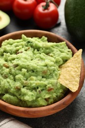 Photo of Delicious guacamole with nachos chips and ingredients on grey table, closeup