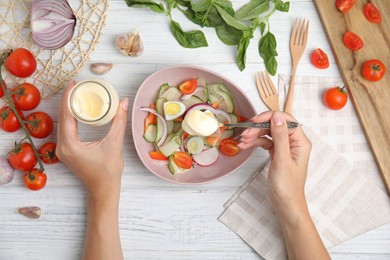 Photo of Top view of woman dressing delicious salad with mayonnaise at white wooden table, closeup