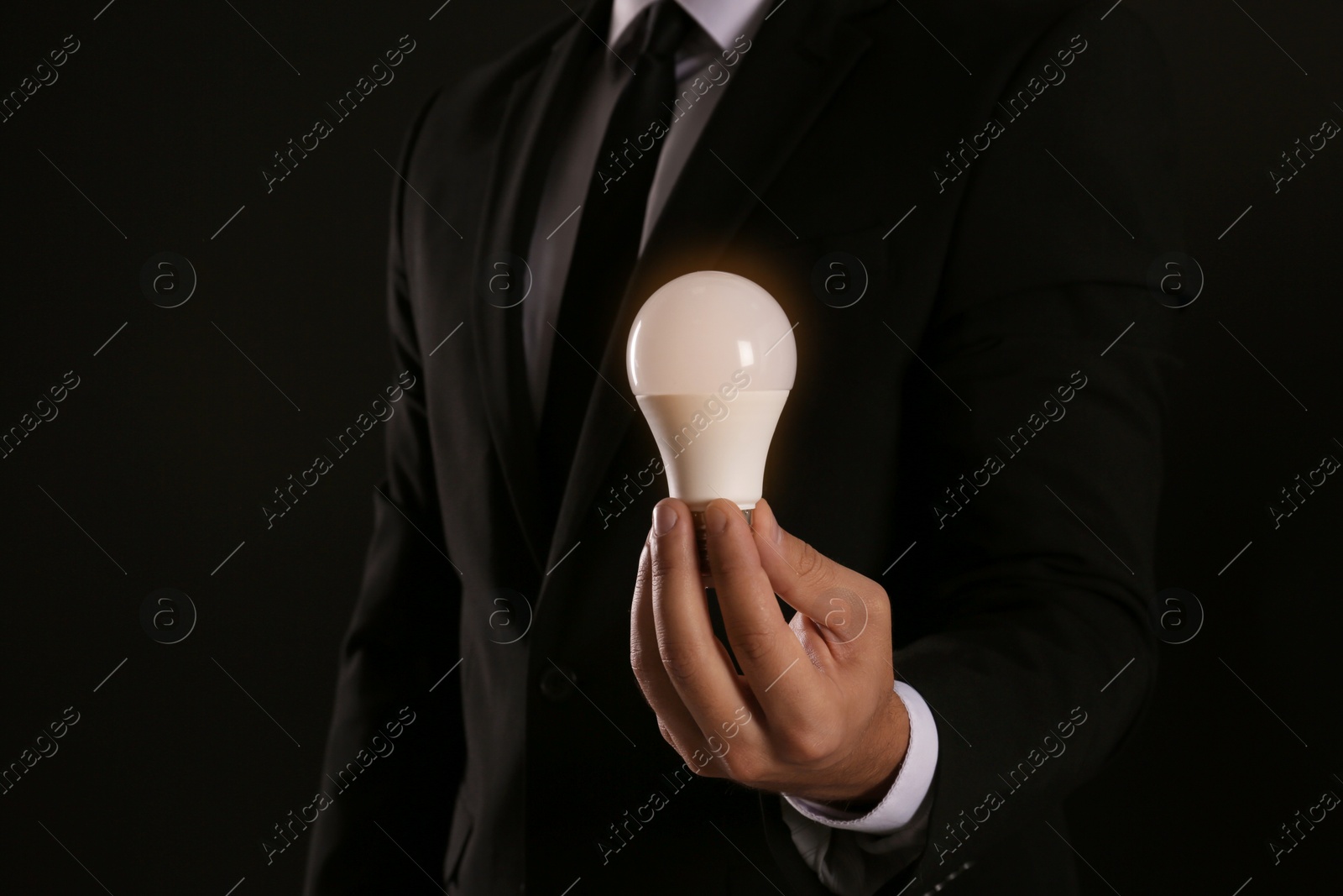 Photo of Businessman holding lamp bulb against dark background