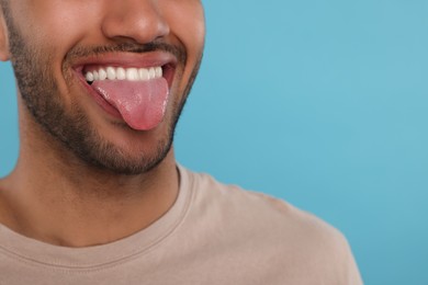 Photo of Happy man showing his tongue on light blue background, closeup. Space for text