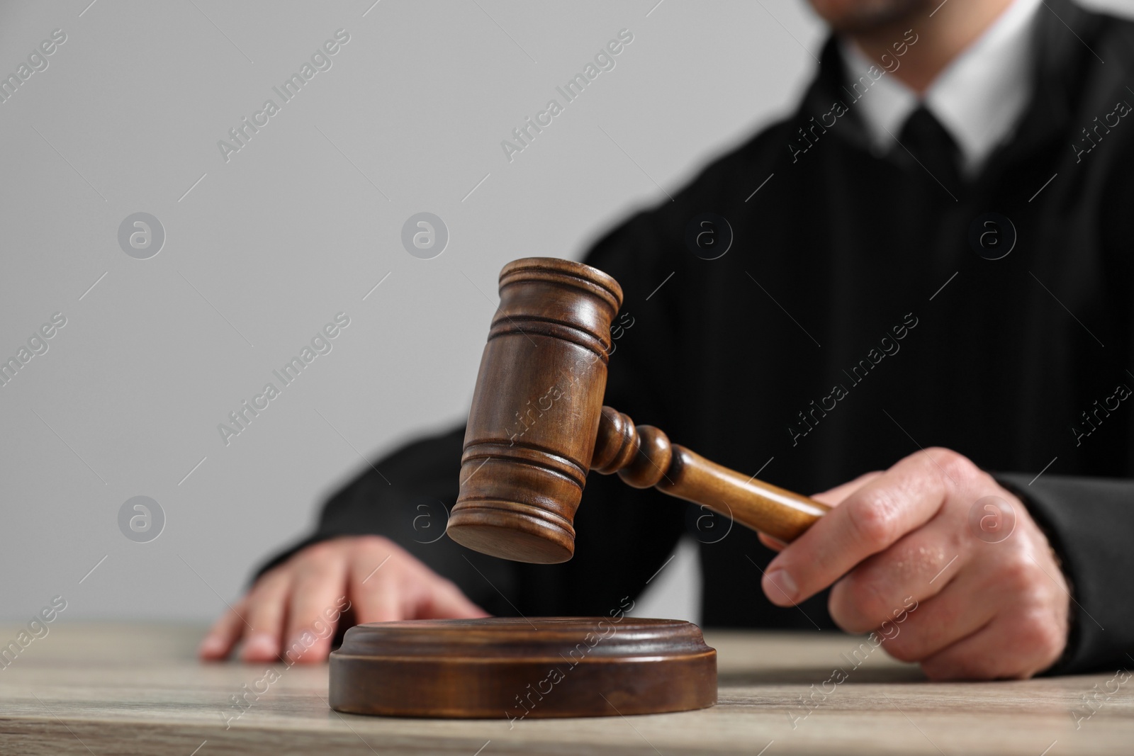 Photo of Judge with gavel sitting at wooden table against light grey background, closeup