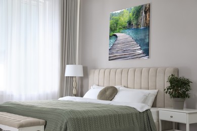 Image of Canvas with printed photo of wooden bridge over lake and waterfall on beige wall in bedroom