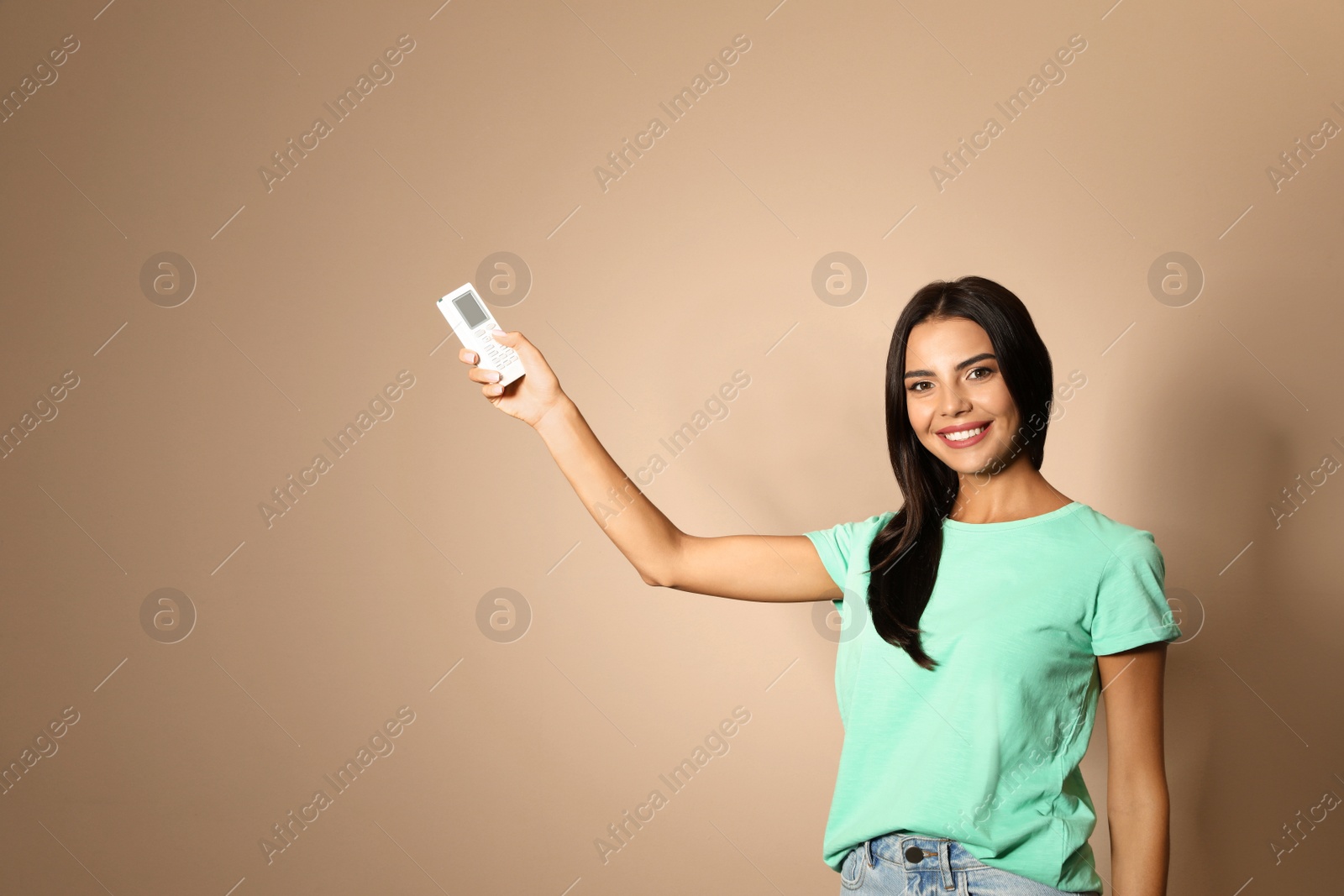 Photo of Young woman with air conditioner remote on beige background. Space for text