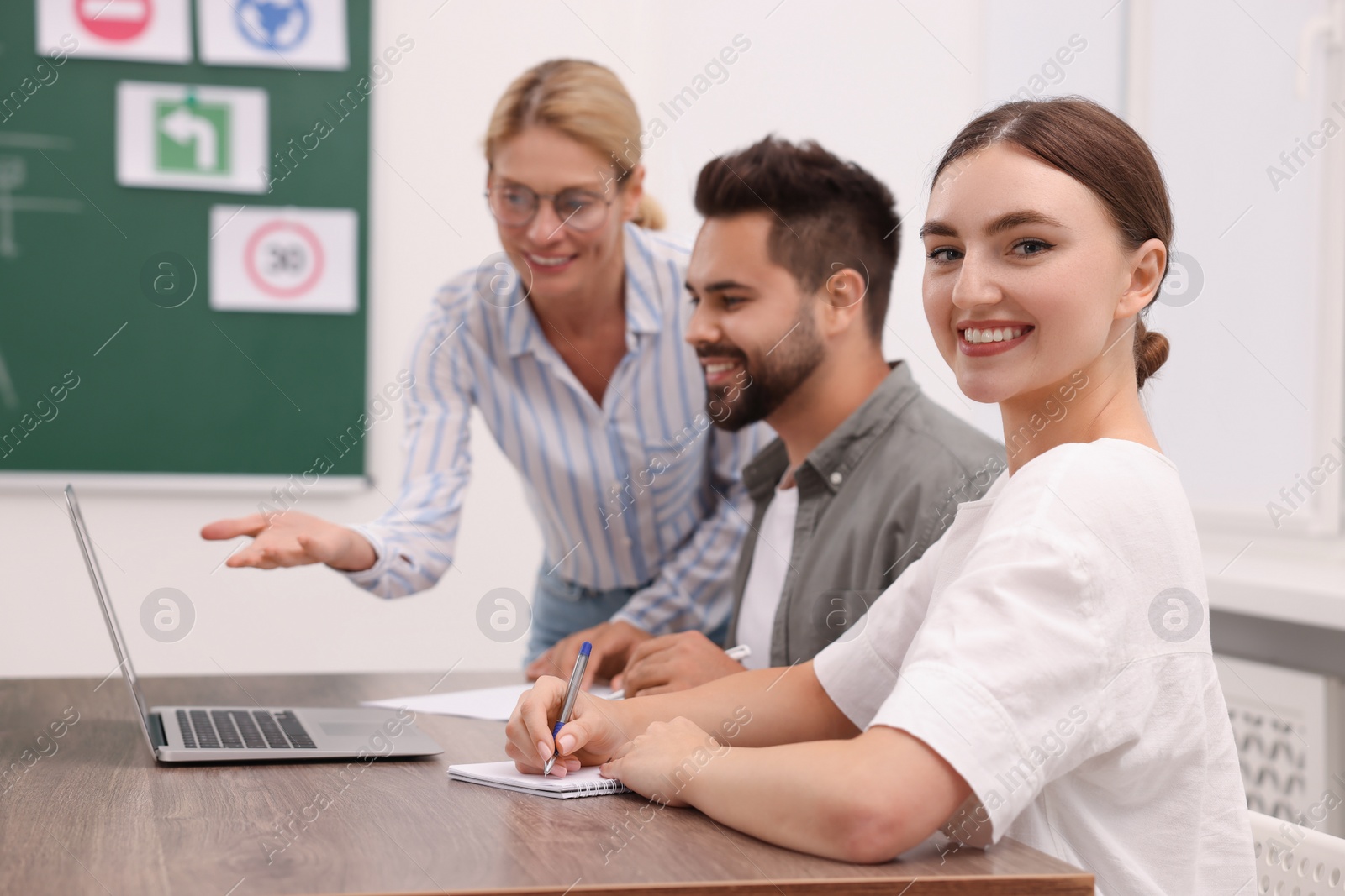 Photo of Happy woman making notes at desk in class during lesson in driving school