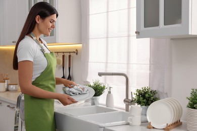 Happy woman wiping plate with towel in kitchen, space for text