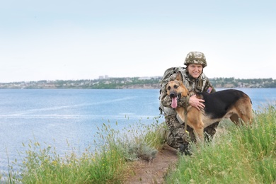 Man in military uniform with German shepherd dog near river