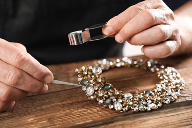 Photo of Male jeweler evaluating necklace at table in workshop, closeup