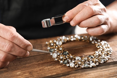 Male jeweler evaluating necklace at table in workshop, closeup