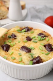 Photo of Tasty sausage casserole with green onions in baking dish served on white table, closeup