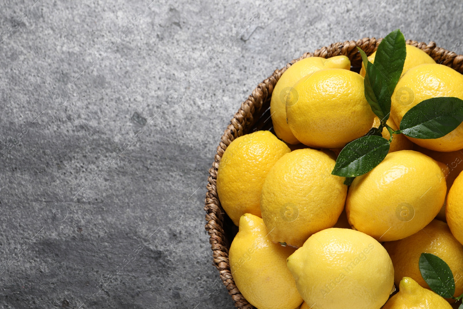 Photo of Fresh lemons in wicker basket on grey table, top view. Space for text