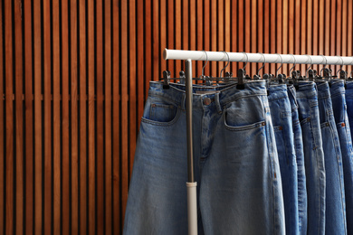 Rack with different jeans on wooden background, closeup. Space for text