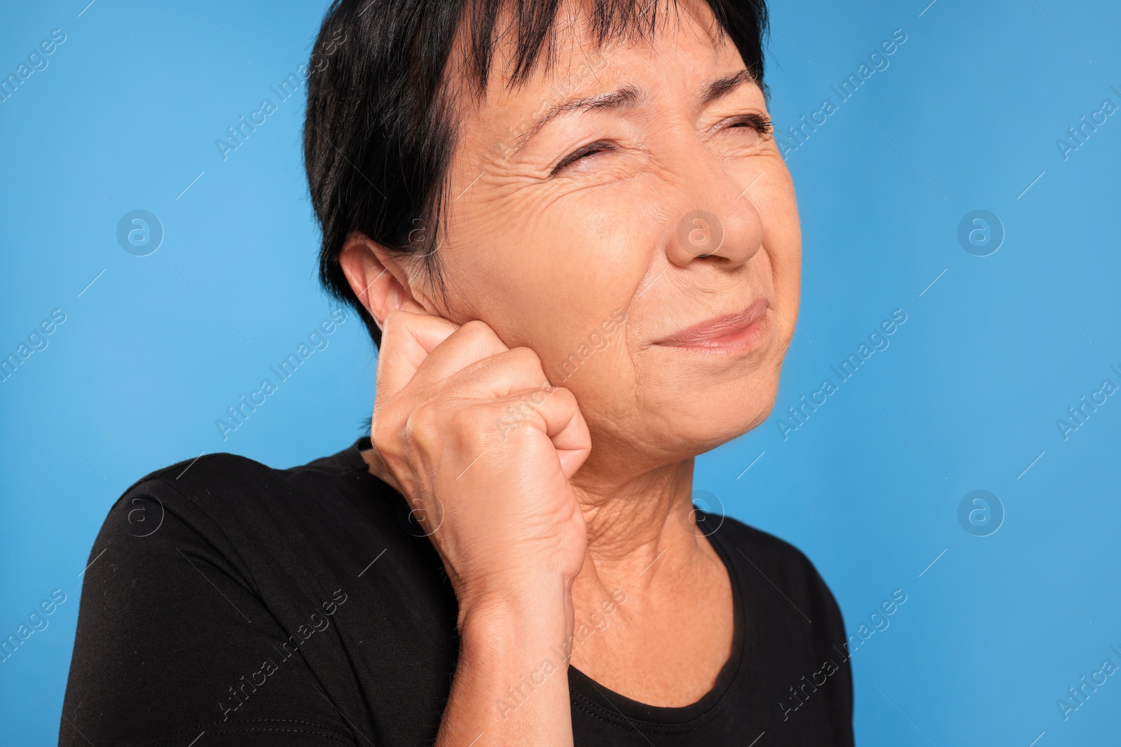 Photo of Senior woman suffering from ear pain on light blue background, closeup