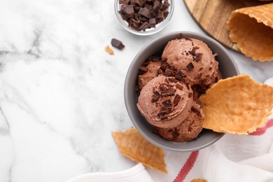 Bowl of tasty ice cream with chocolate chunks and pieces of waffle cone on white marble table, flat lay. Space for text