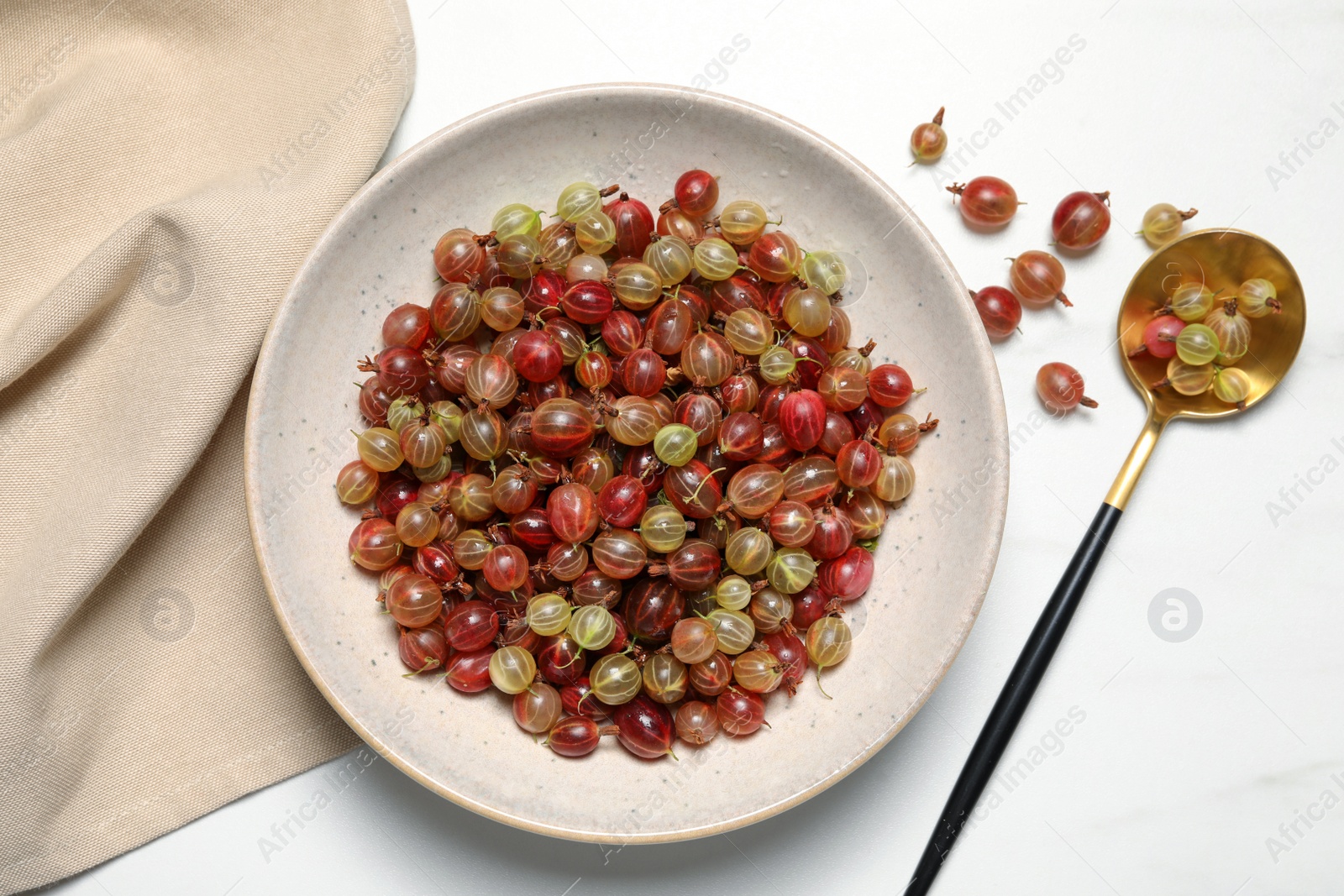 Photo of Fresh ripe gooseberries and spoon on white table, flat lay