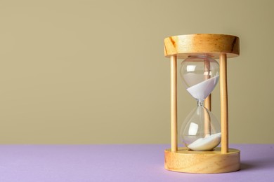 Photo of Hourglass with flowing sand on violet table against beige background, space for text. Menopause concept