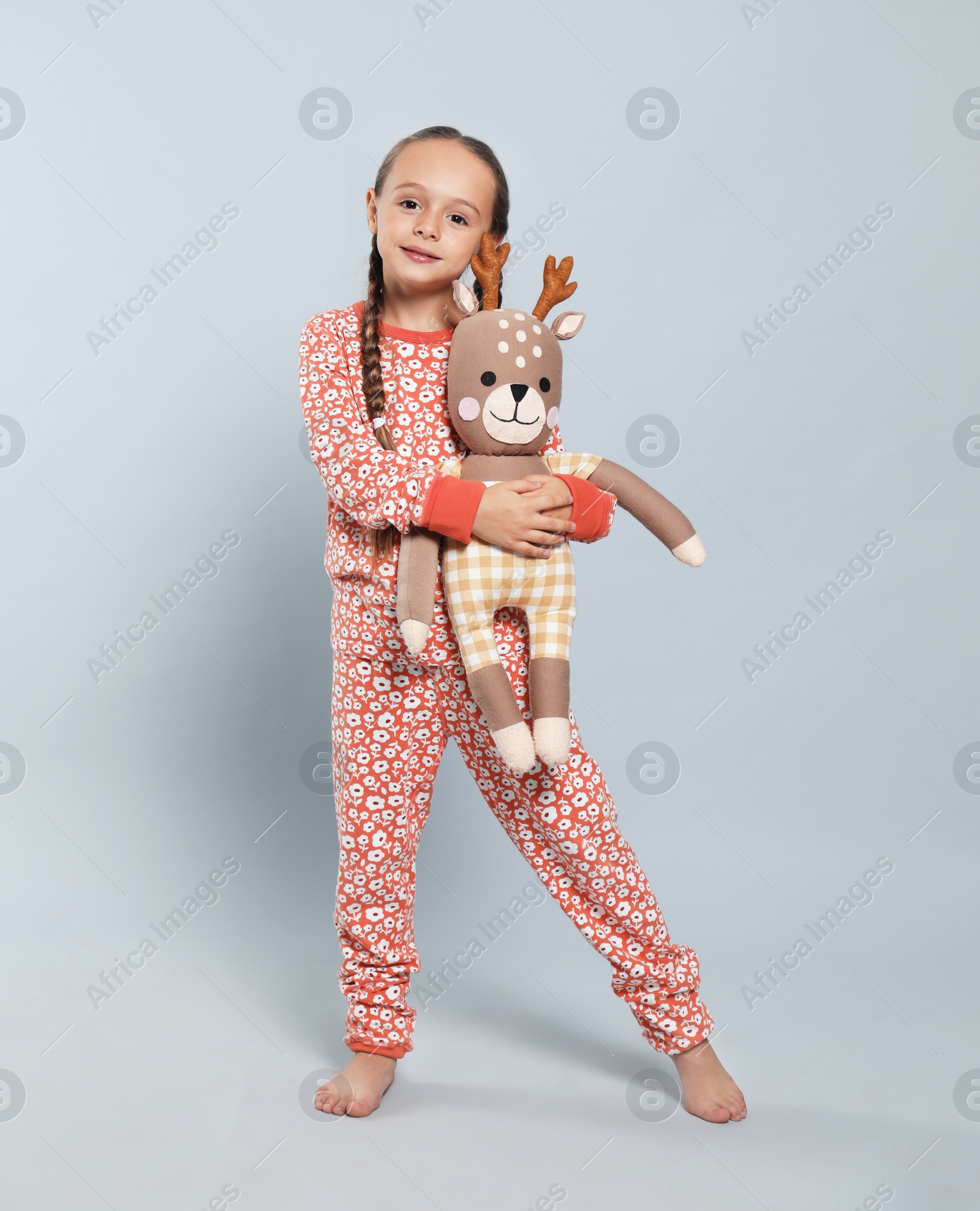 Photo of Cute girl in pajamas with toy deer on light grey background