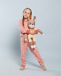 Cute girl in pajamas with toy deer on light grey background