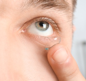 Photo of Young man putting contact lens into his eye, closeup