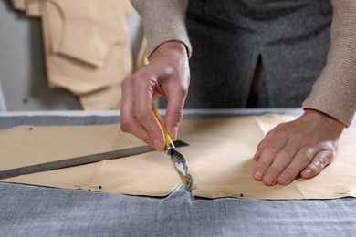 Photo of Tailor transferring sewing pattern onto fabric with tracing wheel in atelier, closeup