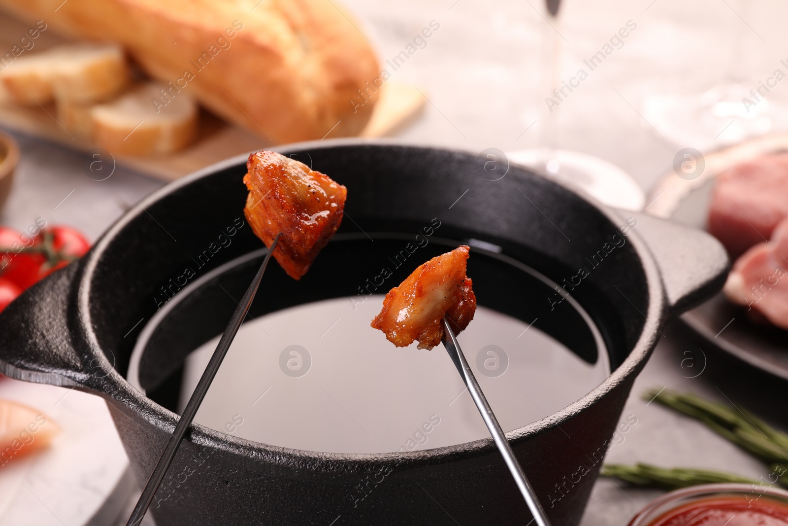 Photo of Fondue pot, forks with fried meat pieces and other products on grey table, closeup