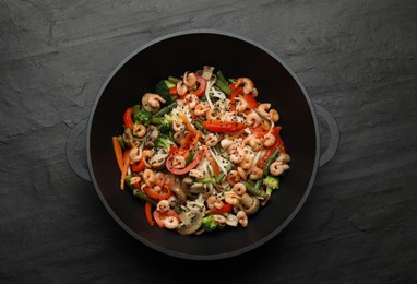 Photo of Stir fried noodles with mushrooms, shrimps and vegetables in wok on black table, top view