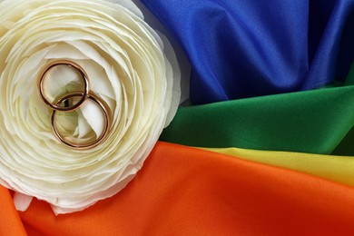 Wedding rings and flower on rainbow LGBT flag, top view