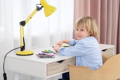 Photo of Boy sitting at desk in room. Home workplace