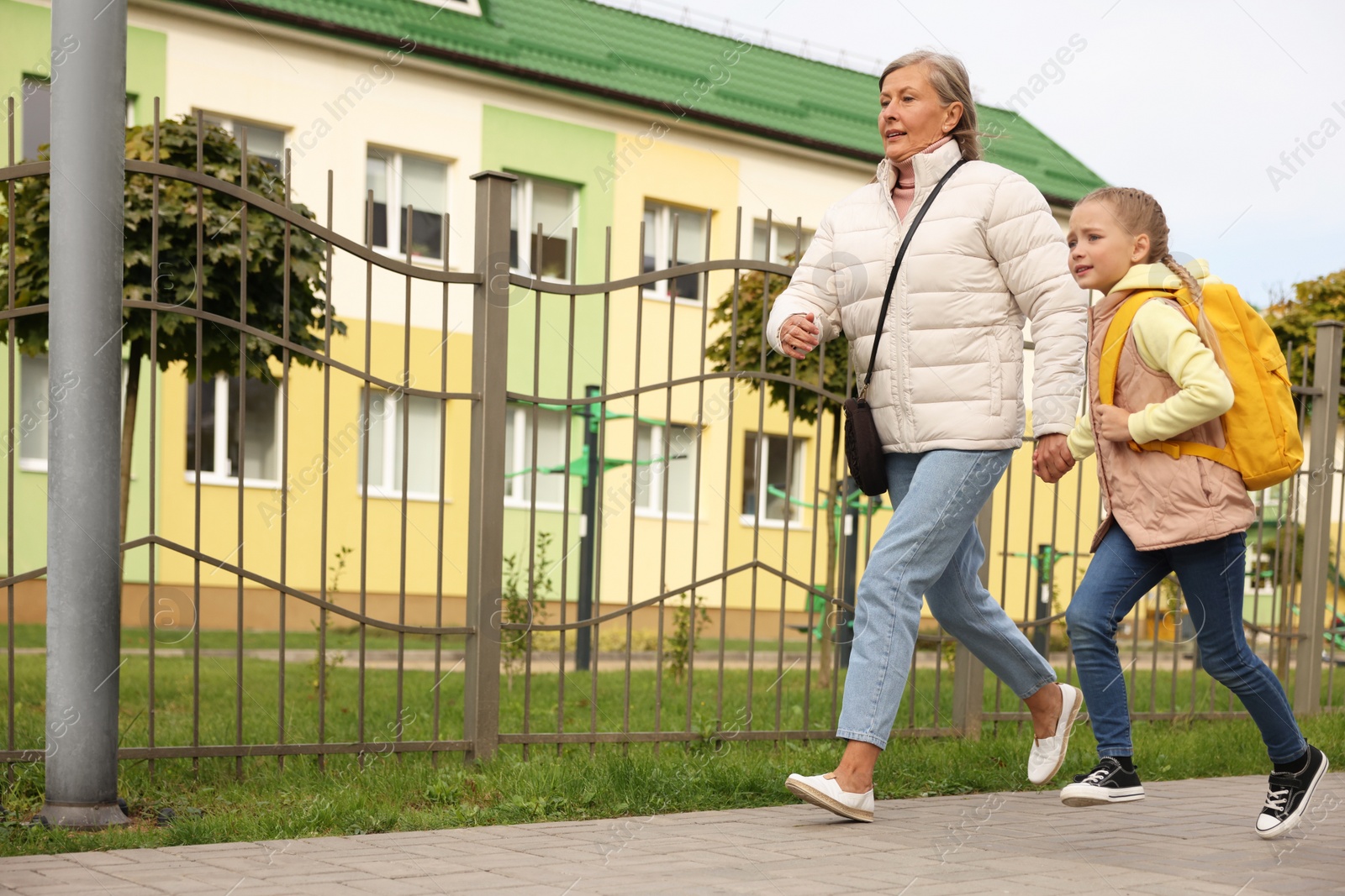 Photo of Being late for school. Senior woman and her granddaughter with backpack running outdoors, low angle view