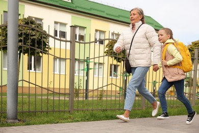 Being late for school. Senior woman and her granddaughter with backpack running outdoors, low angle view