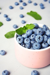 Photo of Cup with juicy blueberries and green leaves on color table