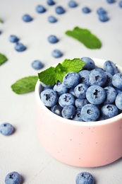 Cup with juicy blueberries and green leaves on color table