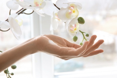 Photo of Young woman applying cream onto hand against window