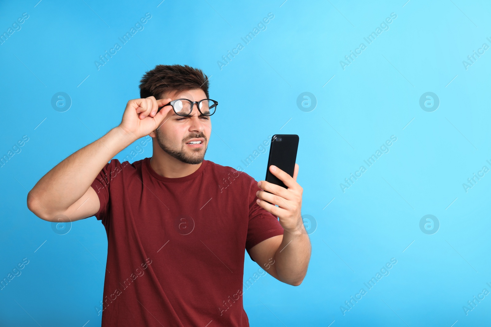 Photo of Young man with vision problems using smartphone on blue background, space for text