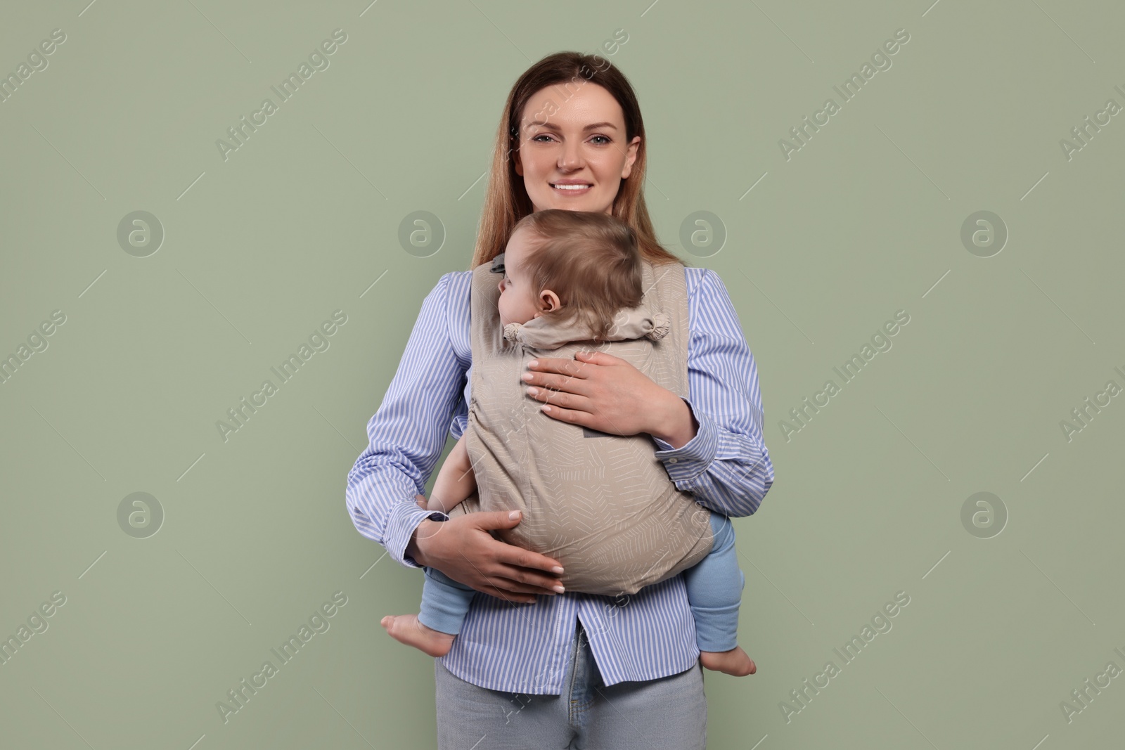 Photo of Mother holding her child in sling (baby carrier) on olive background