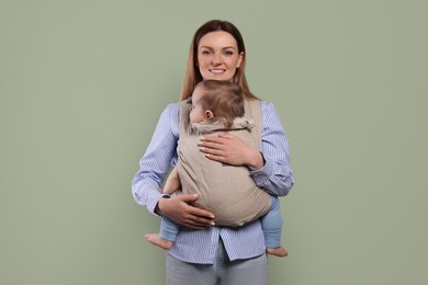 Photo of Mother holding her child in sling (baby carrier) on olive background