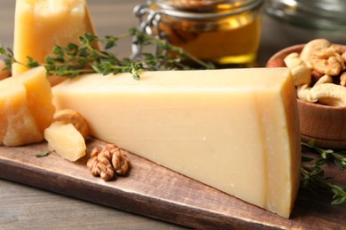 Photo of Delicious parmesan cheese served with honey, walnuts and thyme on wooden table, closeup