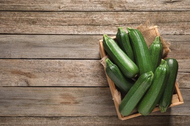 Photo of Raw ripe zucchinis in crate on wooden table, top view. Space for text