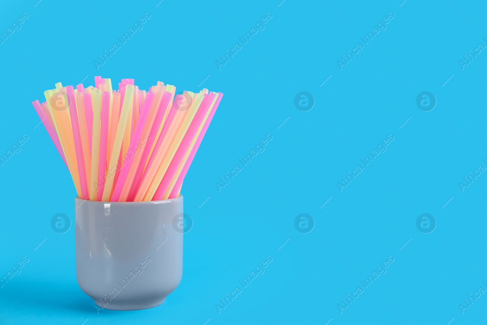 Photo of Colorful plastic drinking straws in holder on light blue background, space for text