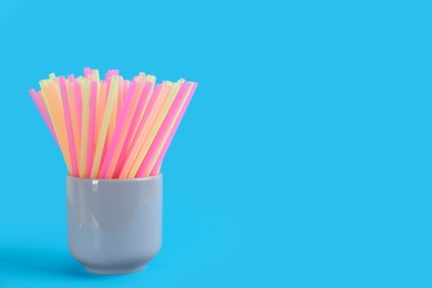 Photo of Colorful plastic drinking straws in holder on light blue background, space for text